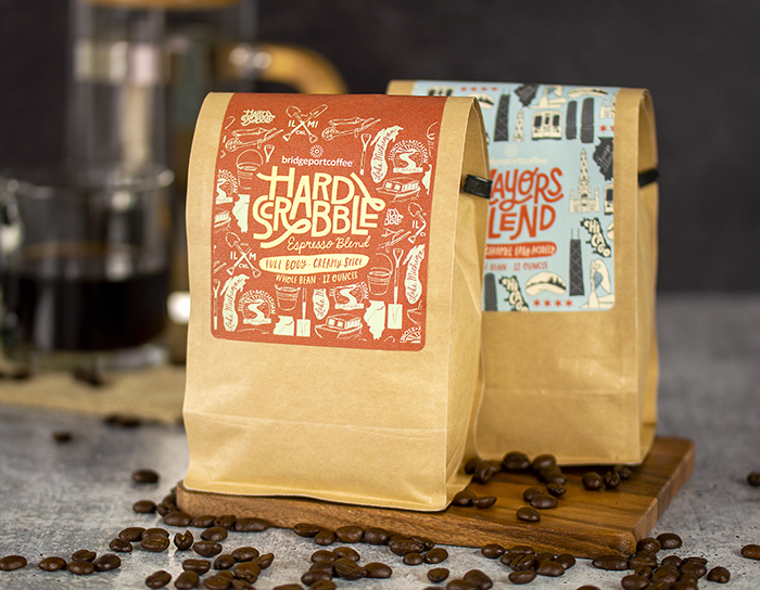 Luxury Estate 9 Roll Labels-Two bags of premium coffee, one with the label 'Hard Scrabble Espresso Blend' and the other 'Lawyers Blend', displayed on a wooden surface with scattered coffee beans. The labels boast a rustic design with intricate illustrations, suggesting a luxurious and traditional feel. The kraft paper packaging enhances the vintage appeal and suggests high-quality contents.